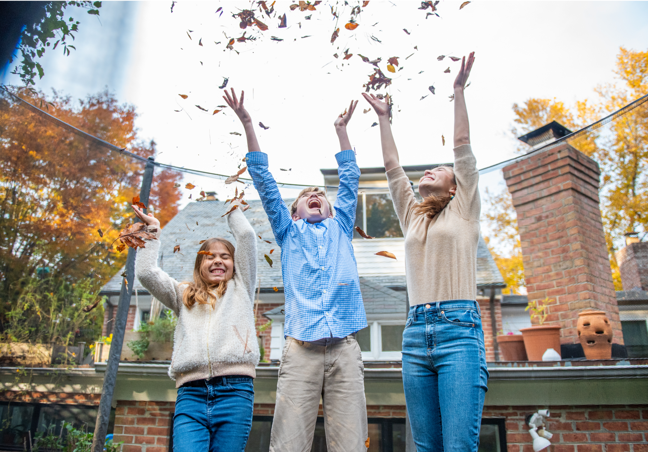 Three children outside throwing leaves into the air